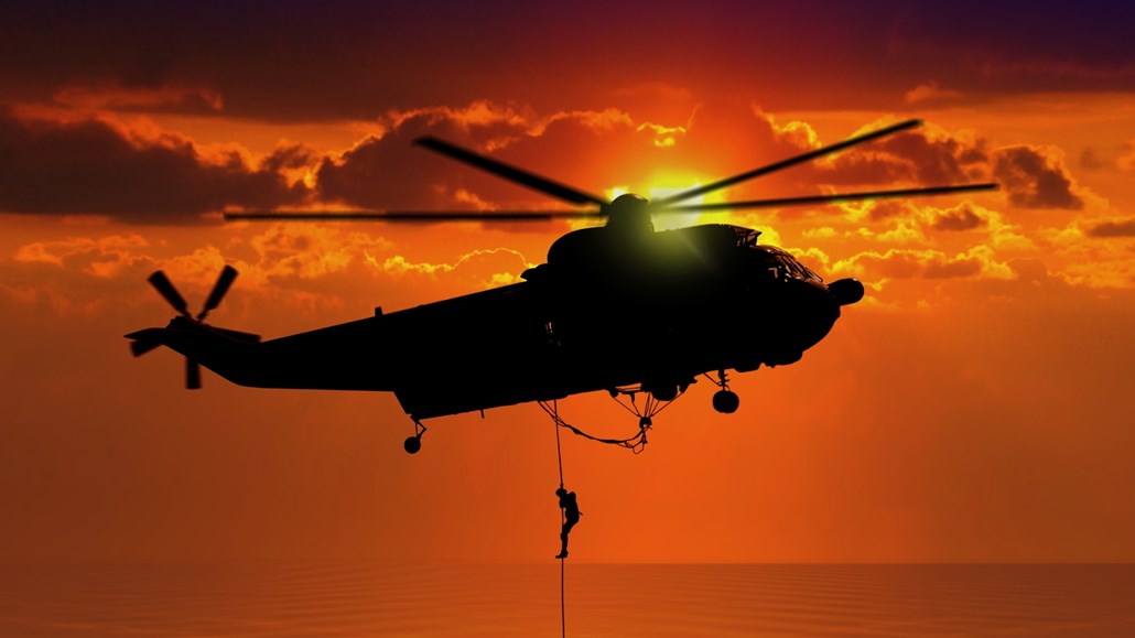 helicopter flying through sky with man hanging off rope