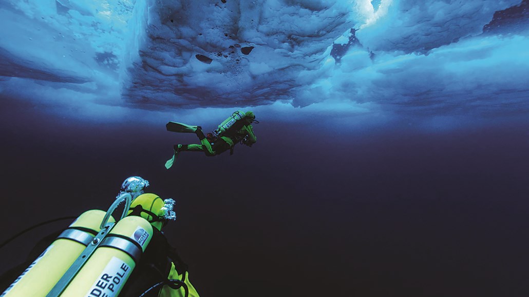 two scuba divers swimming under icy water